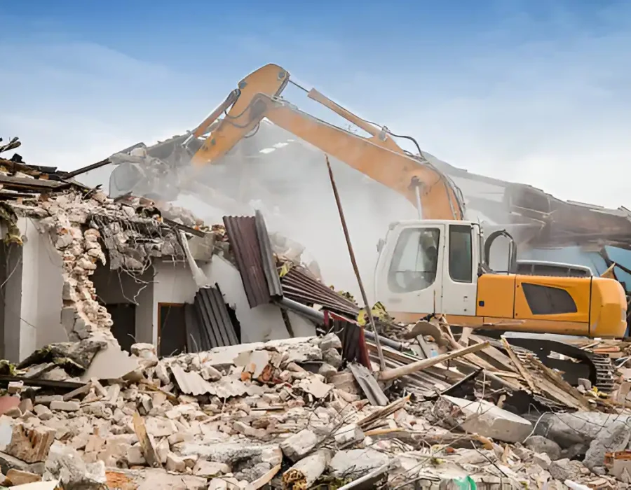 Excavator dismantling white structure with massive concrete and debris pile
