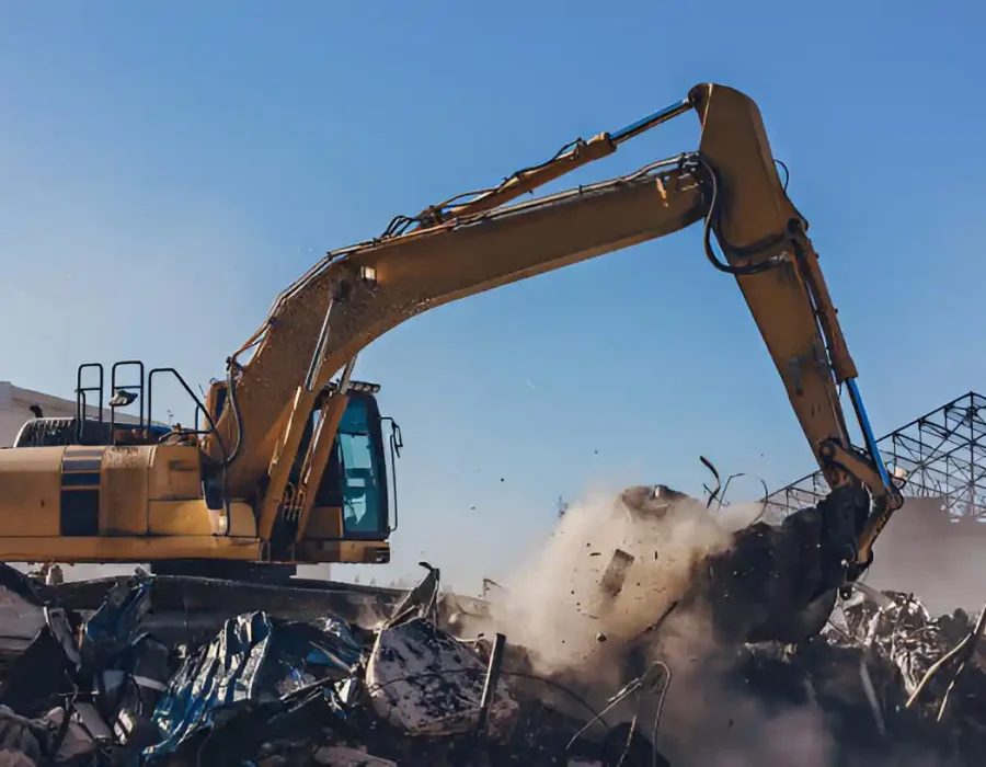 Yellow excavator sorting and moving metal scrap at demolition site