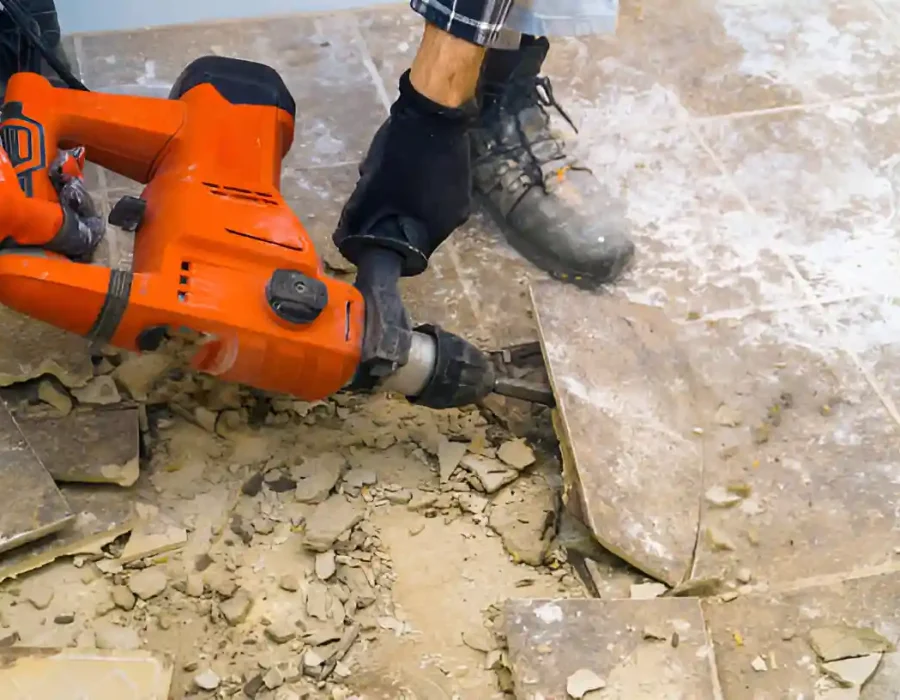 Industrial jackhammer breaking up floor tiles during demolition with debris cleanup and site preparation