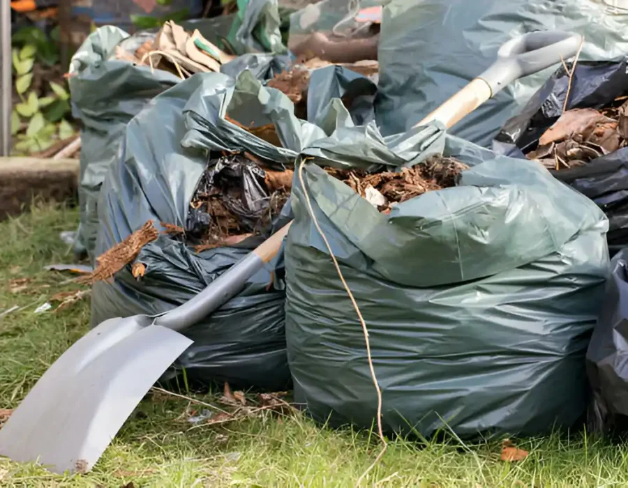 Green waste bags filled with yard debris and shovel on lawn ready for professional removal service
