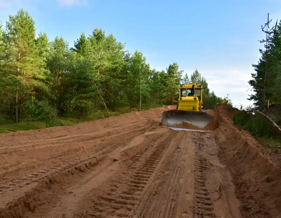 Yellow bulldozer grading dirt road through forested area for construction site preparation