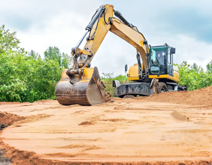 Excavator moving sand for debris removal and construction site preparation in wooded area