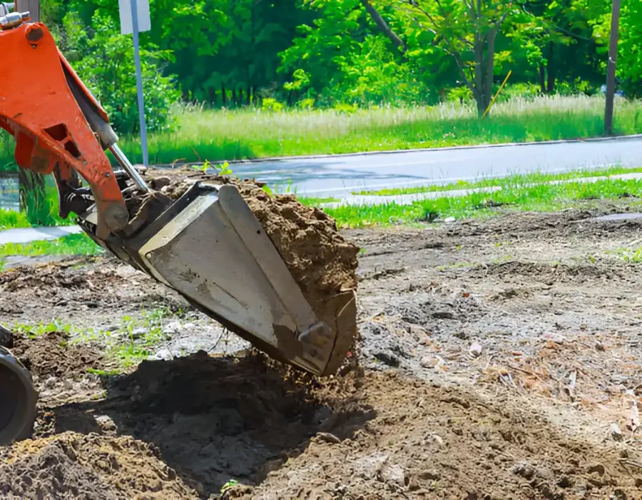 Excavator bucket lifting soil for debris removal and site preparation near road area