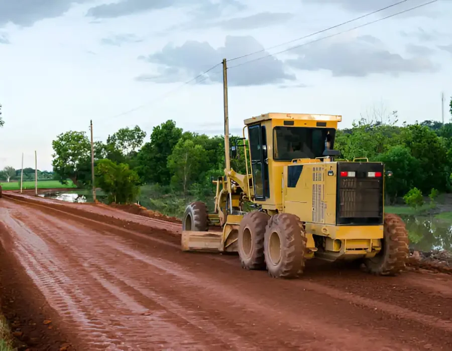 Heavy-duty motor grader performing site preparation and ground leveling on red clay soil for construction project