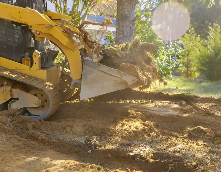 Excavator bucket lifting soil and debris for site preparation in residential area