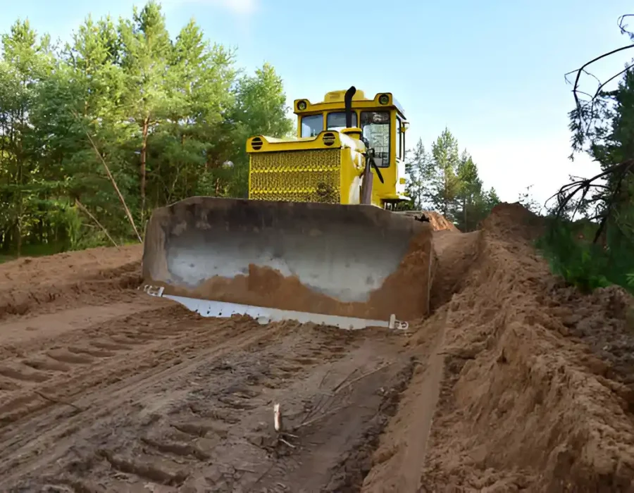 Industrial yellow bulldozer performing land clearing and site preparation in wooded area for demolition project