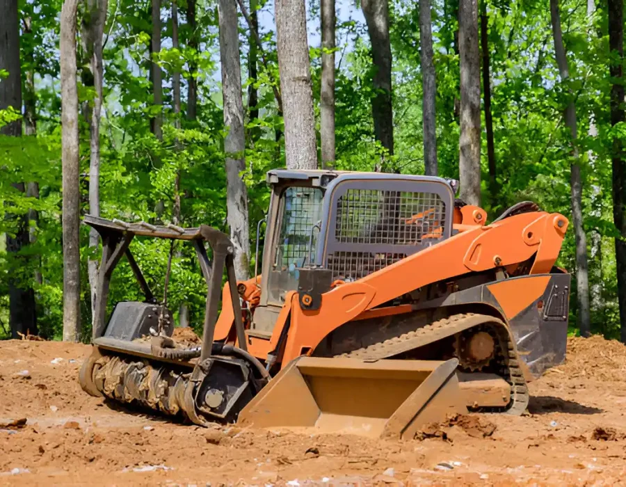 Skid steer loader moving dirt for debris removal and site cleanup in wooded area