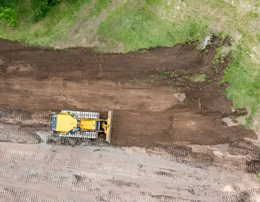 Grader leveling dirt for site cleanup and debris removal in construction area from above