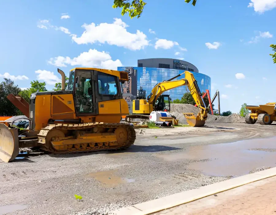 Heavy demolition machinery including bulldozer and excavator preparing commercial site with office building backdrop