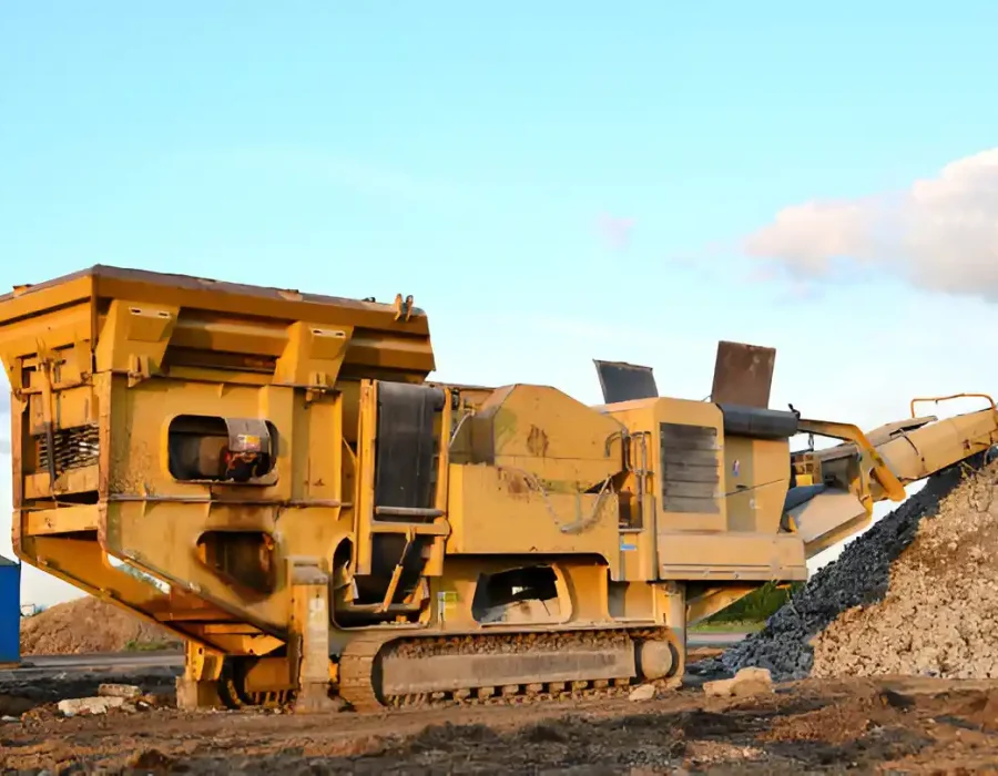 Yellow crusher machine processing rubble at a demolition site under a clear sky.