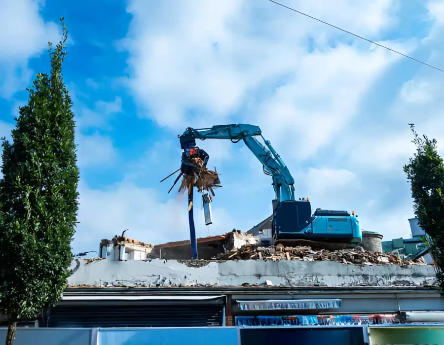 Blue excavator with grapple attachment removing debris from commercial building rooftop