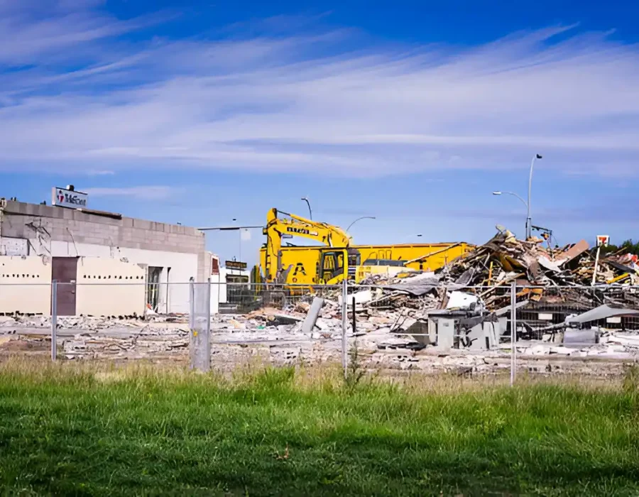 Wide view of retail building demolition site with yellow excavators and secured perimeter