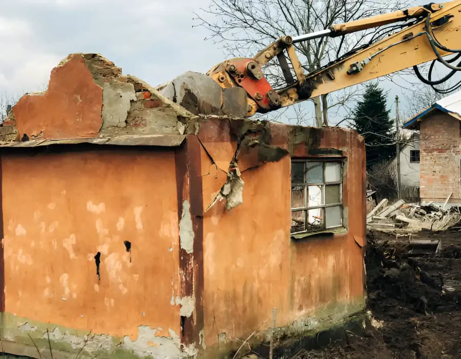 Excavator arm demolishing orange brick wall of abandoned house during structural teardown