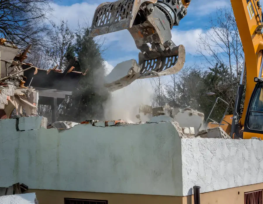 Excavator with sorting grapple demolishing concrete wall structure with dust control measures