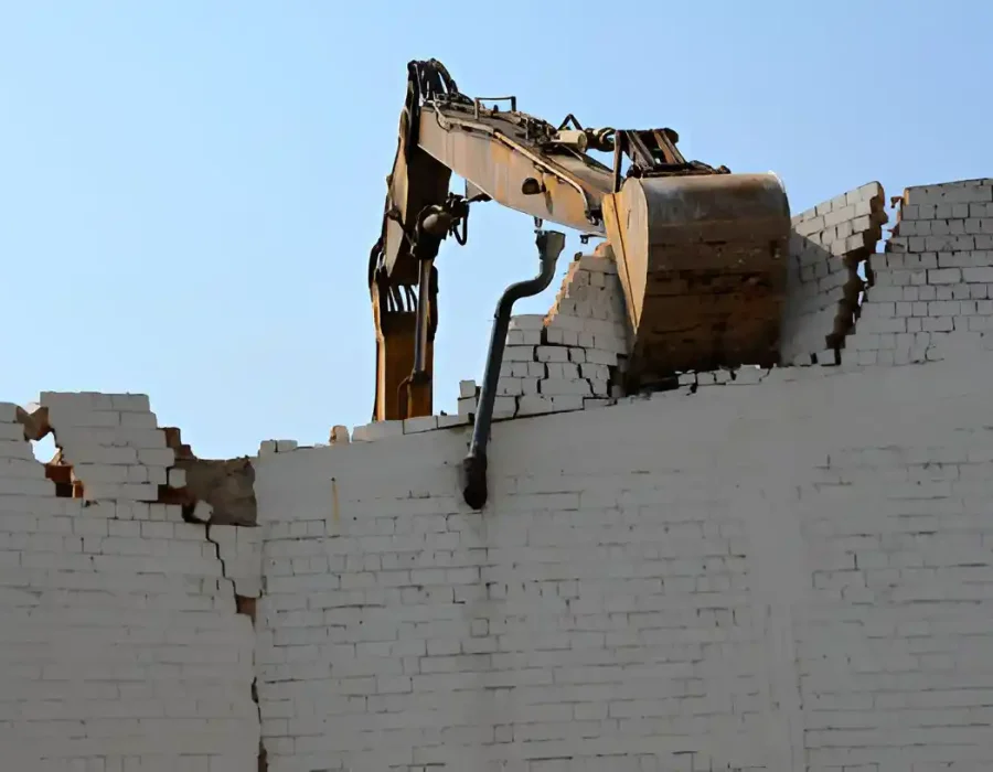 Excavator bucket breaking down white brick wall during precision demolition work