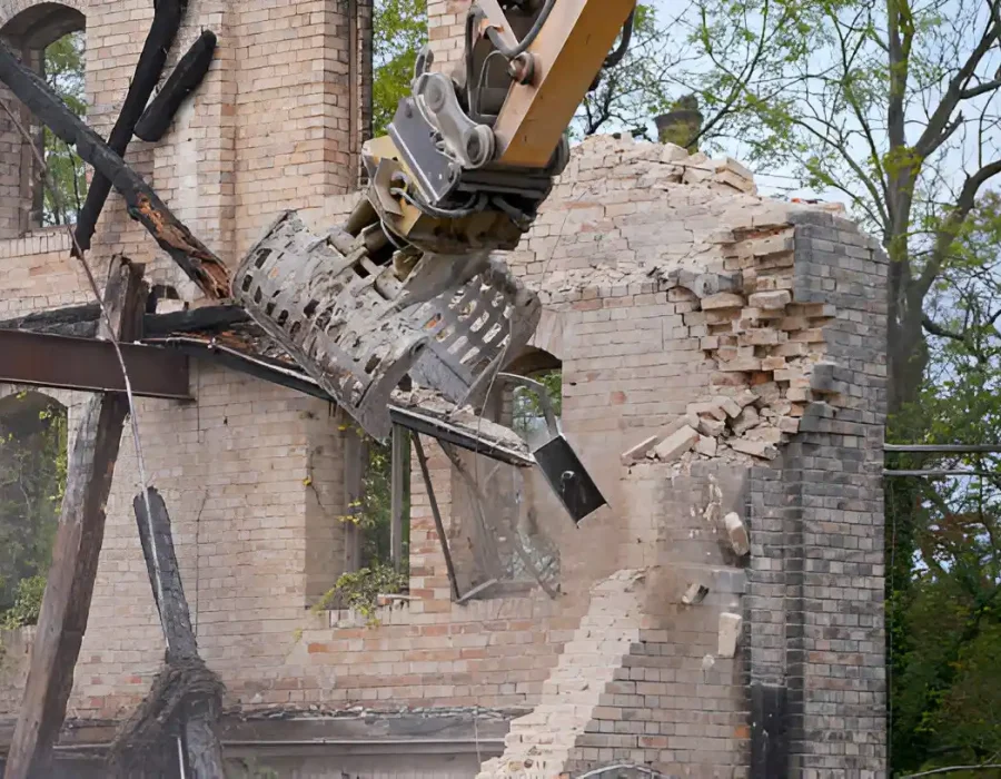 Excavator with sorting grapple demolishing vintage brick wall structure with precision control