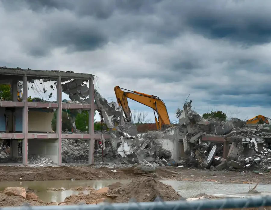 Excavator demolishing concrete frame building with exposed structure and debris piles