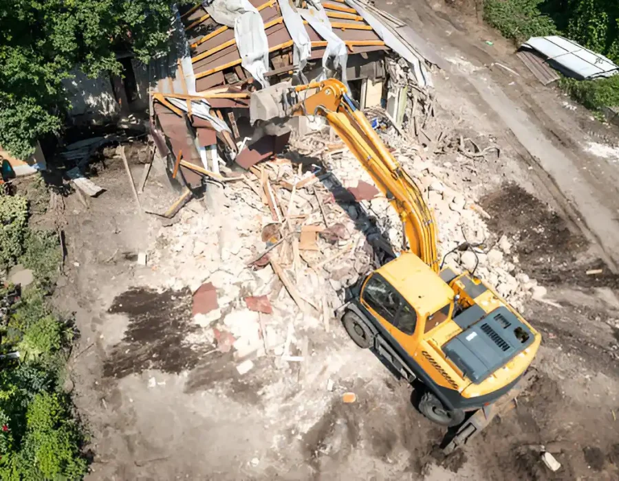 Bird's eye view of yellow excavator demolishing building structure with scattered debris