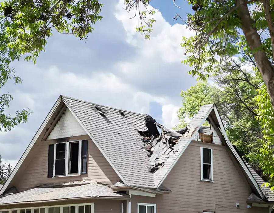 Damaged residential roof with collapsed section, tree-lined background, repair needed