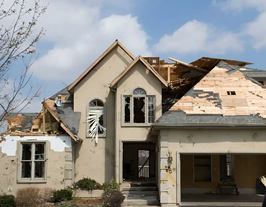 Partially destroyed residential house, roof torn off, windows broken, debris visible