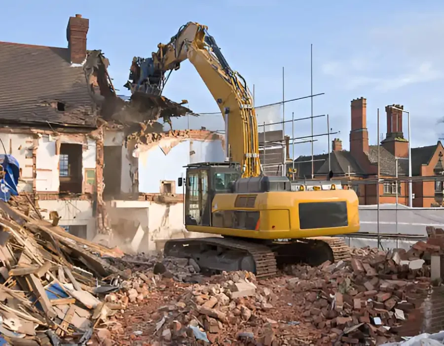 Yellow excavator destroying brick house, wooden debris, urban demolition site