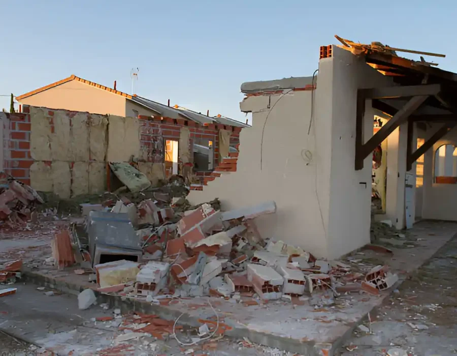 Partially demolished house with scattered debris and rubble on the ground.