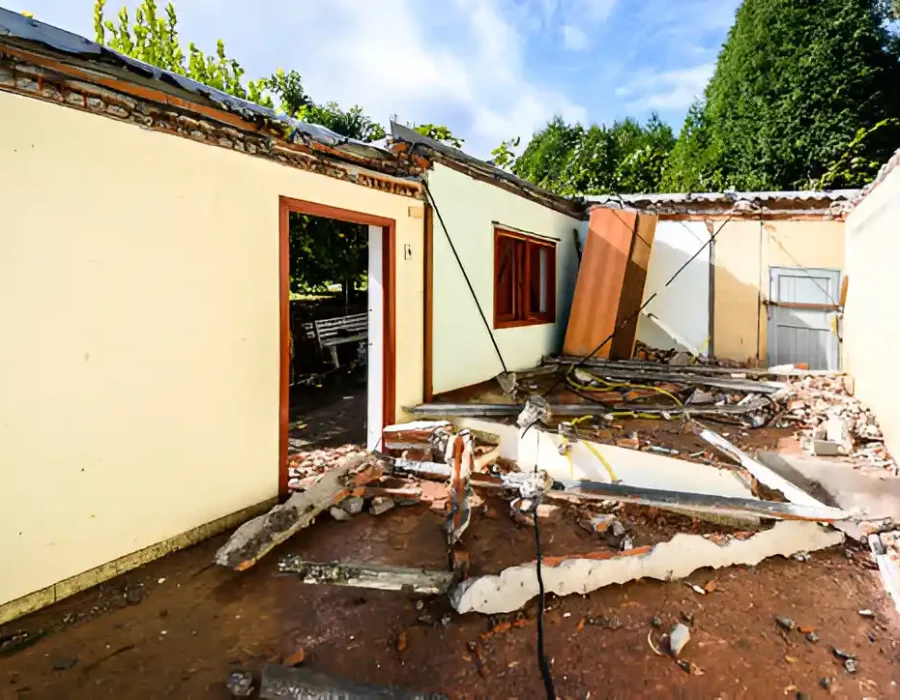 Yellow excavator demolishing multi-story brick building, creating massive debris pile