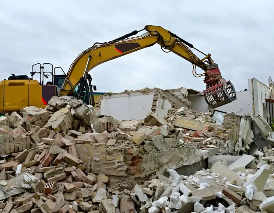 Yellow excavator with sorting grapple managing building demolition waste and rubble