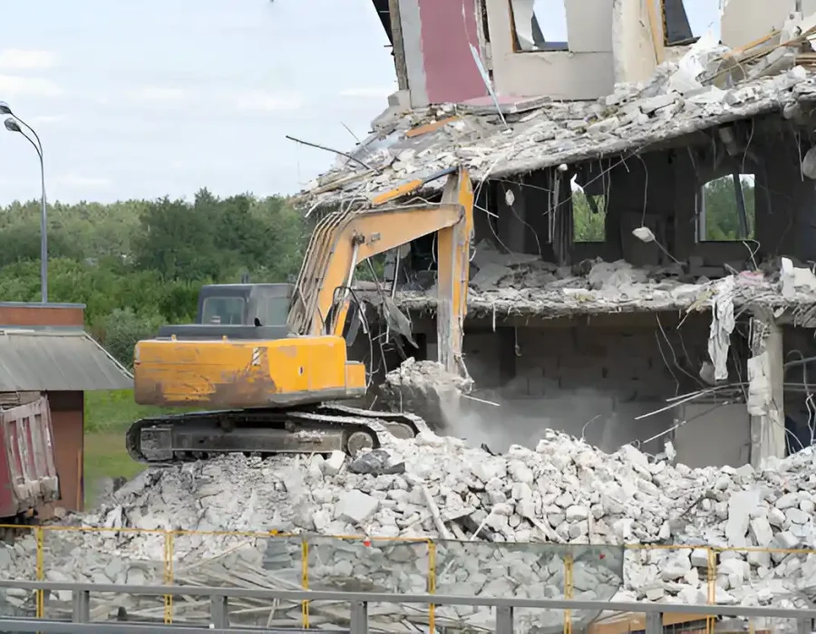 Yellow excavator dismantling concrete structure, urban demolition site with debris removal