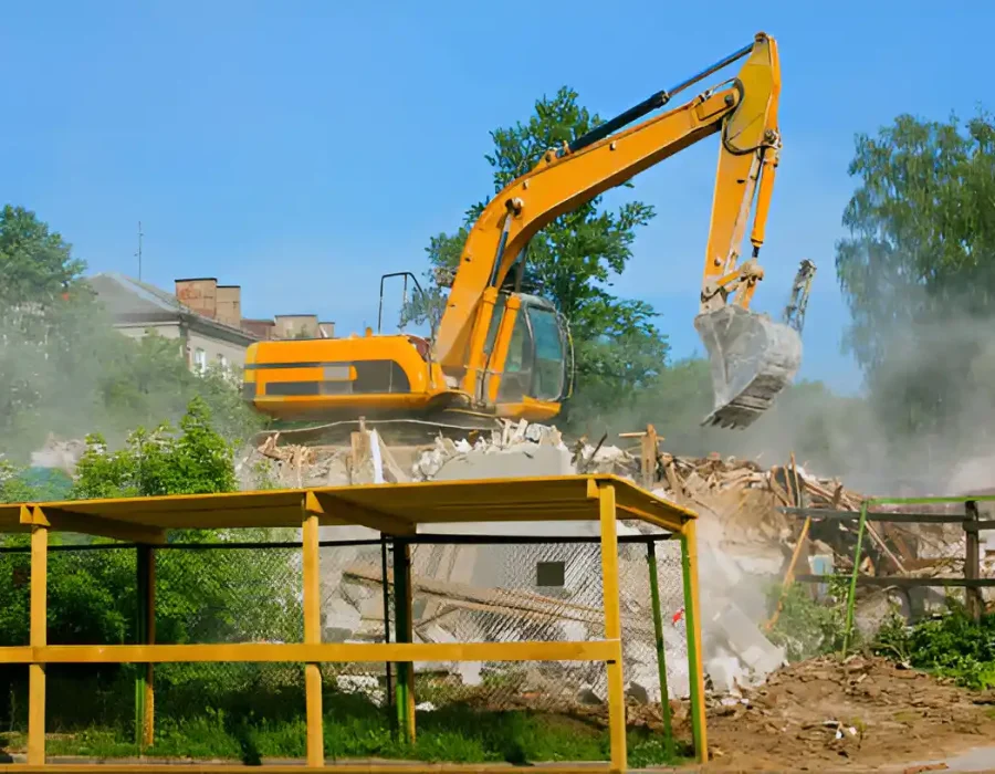 Yellow excavator breaking down structures with dust, professional demolition site cleanup
