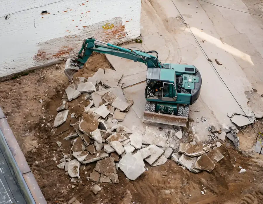 Teal wheeled excavator breaking concrete slab, professional demolition and debris removal