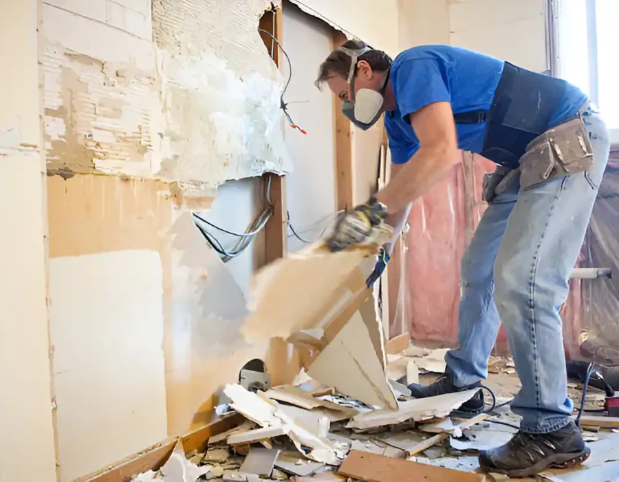 Worker in safety gear removing drywall, residential renovation demolition process