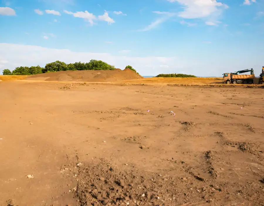 Cleared land with dump truck and excavator for site preparation under a clear sky.