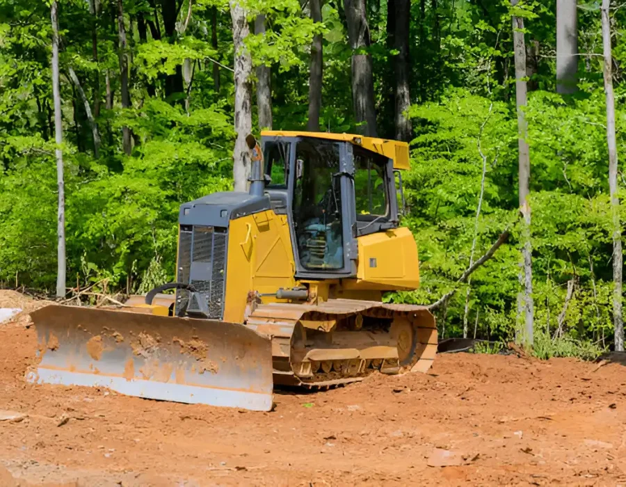 Yellow bulldozer leveling soil for site preparation in a wooded area.