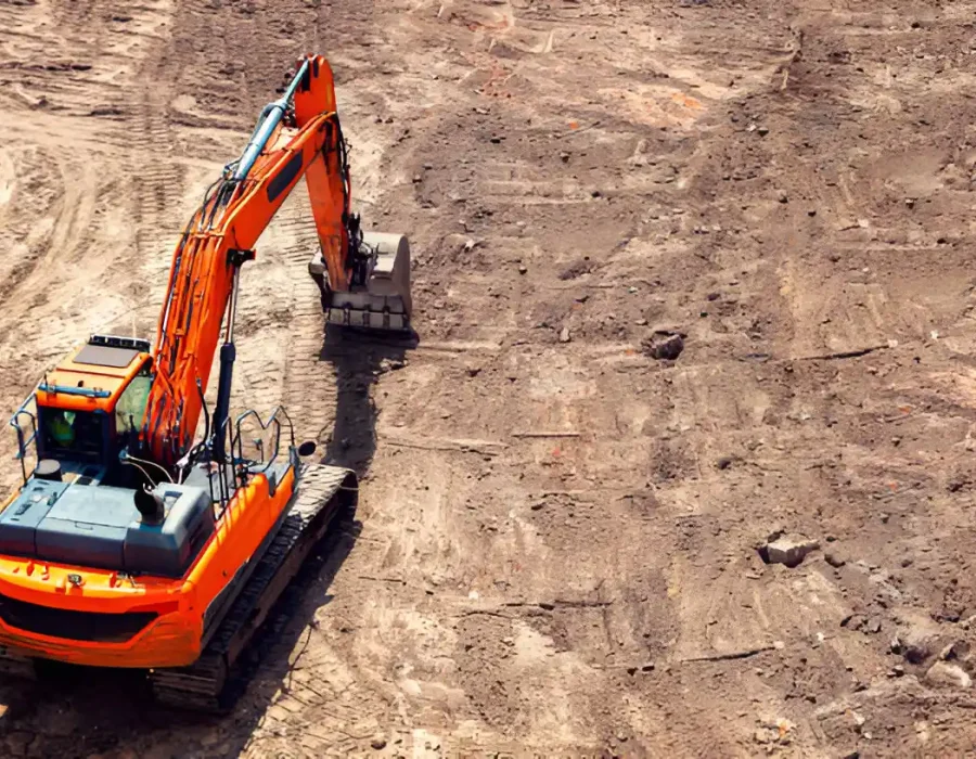Orange excavator leveling soil for site preparation and debris removal.