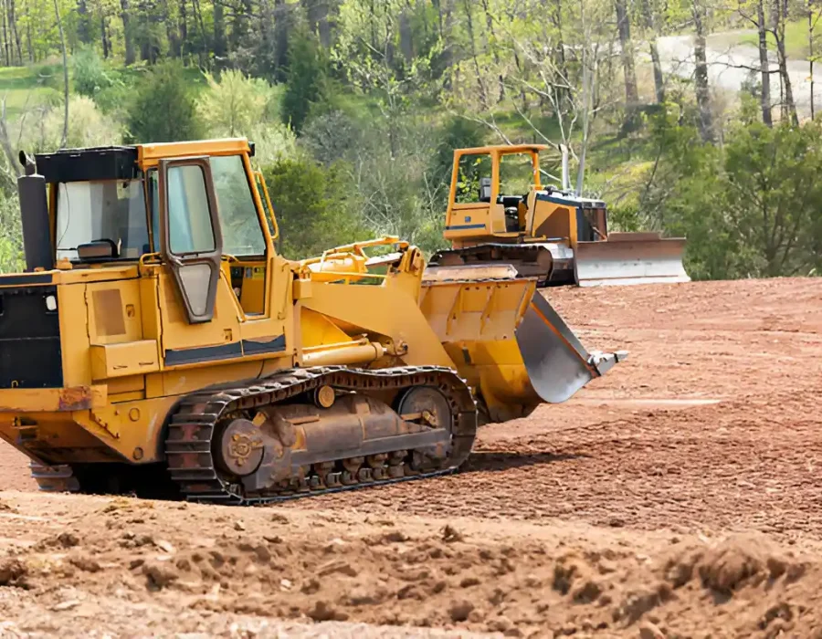 Two yellow bulldozers grading red soil with forested background, heavy machinery at work