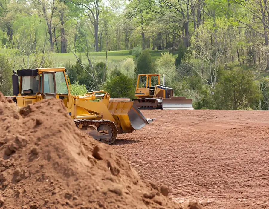 Bulldozers leveling soil on a construction site surrounded by trees and rural houses.
