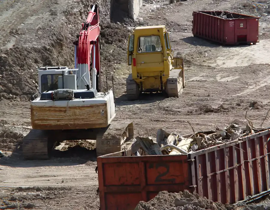 Yellow bulldozer and red excavator working near dumpsters on demolition site with debris