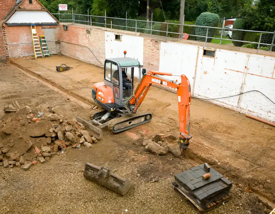 Orange mini excavator clearing construction site rubble and demolition waste