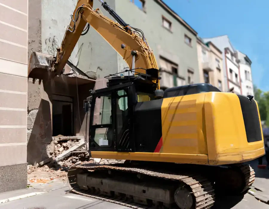 Yellow excavator performing precise demolition work on urban residential building in confined space