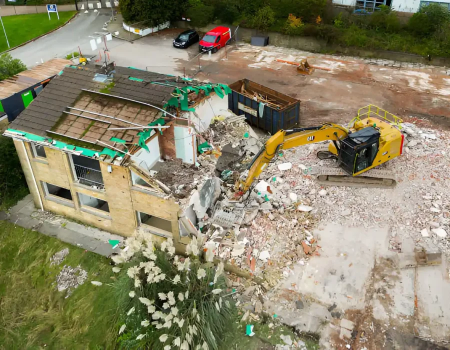 Aerial shot of excavator demolishing single-story building with debris collection and sorting in progress