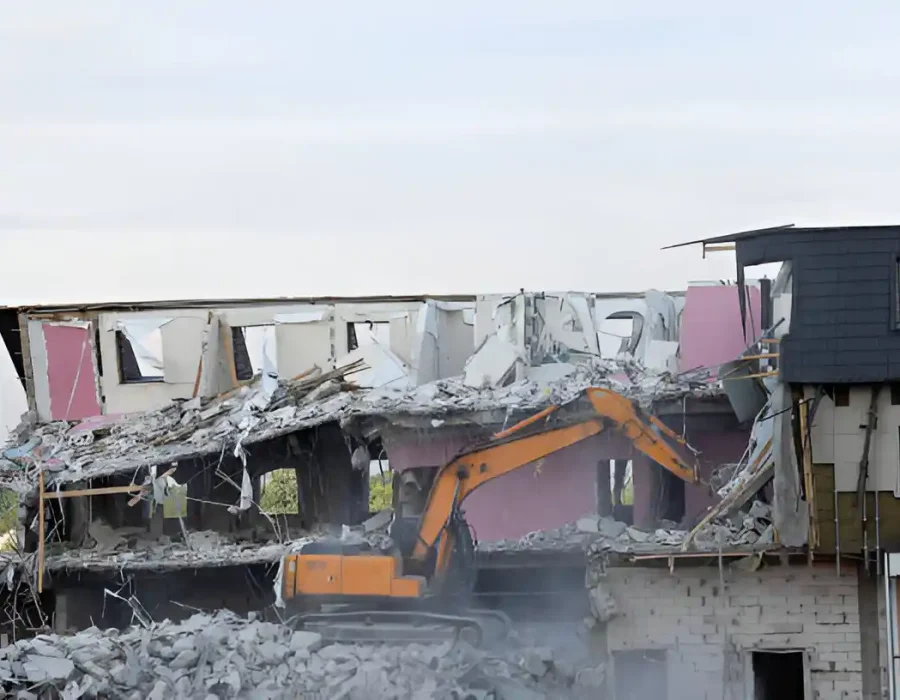 Orange excavator demolishing multi-story residential building with concrete debris and structural removal