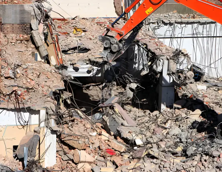 Close-up of demolition site showing mixed construction debris and excavator arm during structural removal