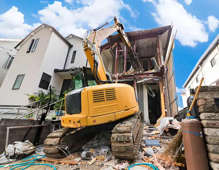 Yellow mini excavator performing precise house demolition between existing residential structures