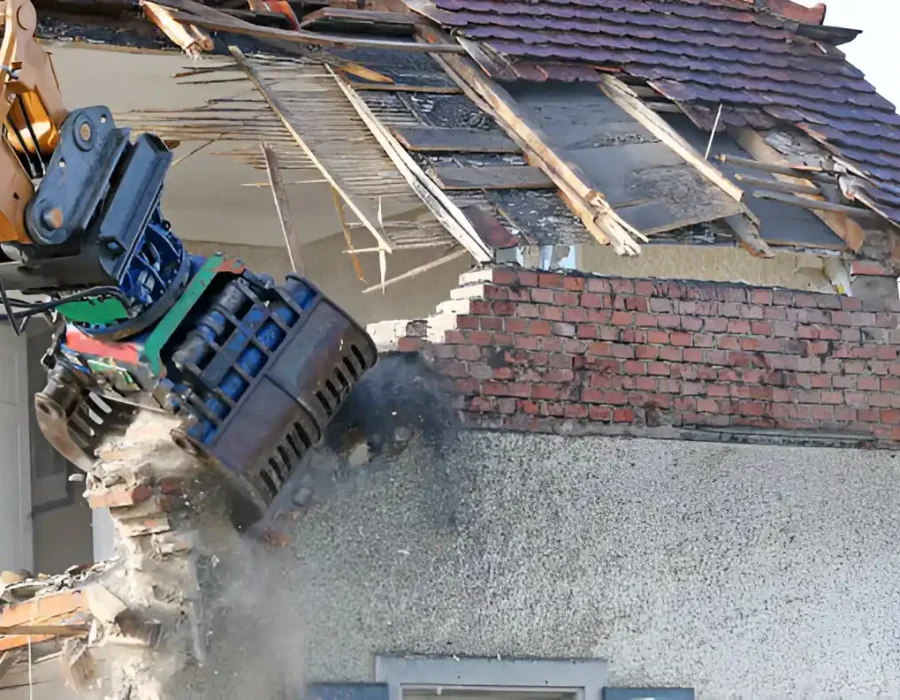 Excavator demolishing white commercial building with exposed structural elements and debris containment