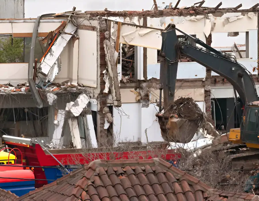 Excavator demolishing white commercial structure with selective debris collection and sorting
