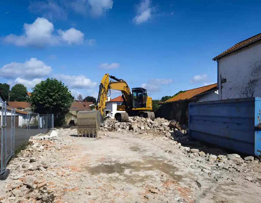 Yellow excavator clearing demolition rubble and concrete debris from cleared construction site