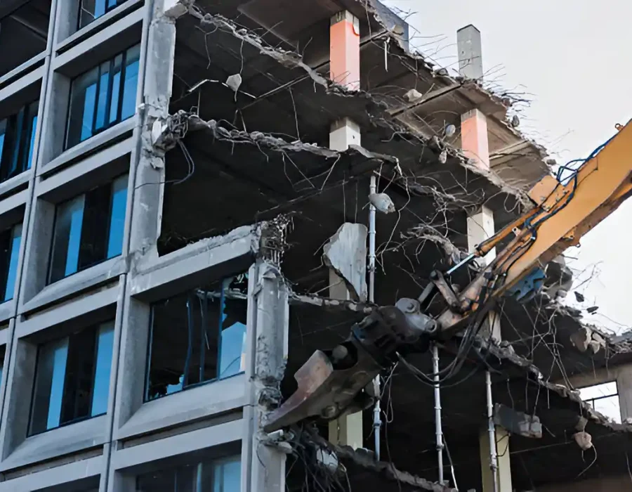 Excavator demolishing multi-story commercial building with exposed structural elements and glass facade