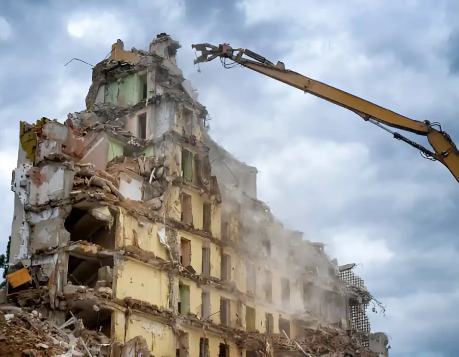 Demolition crane dismantling partially collapsed high-rise building with dust control measures in place