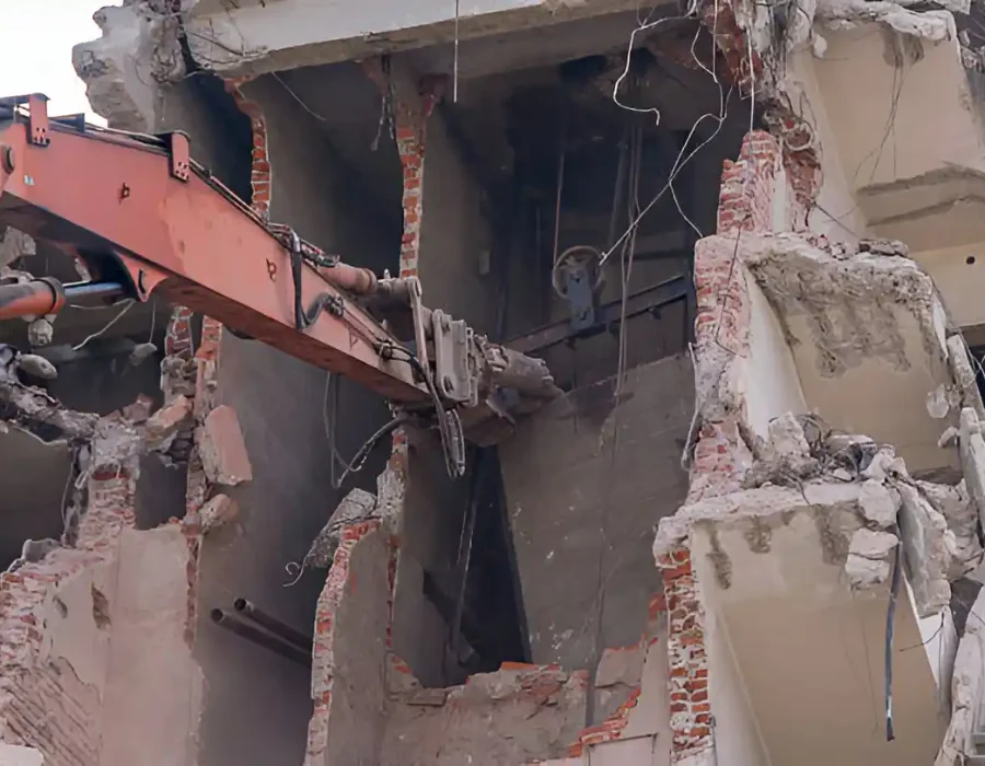 Close-up of demolition equipment breaking through brick and concrete interior walls during building removal